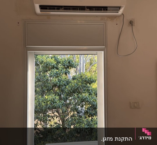 מזגן מותקן מעל חלון עם נוף עצים